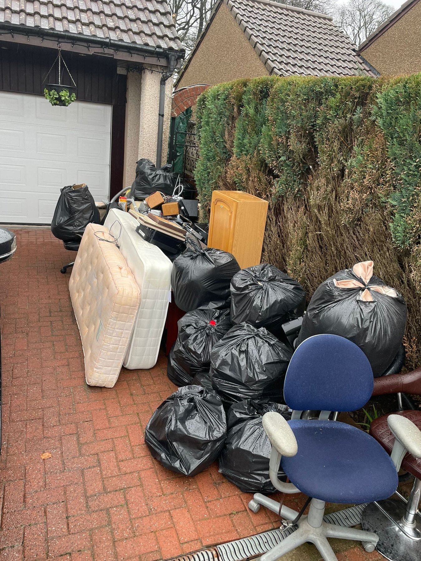 Black bags, mattresses and office chairs gathered on a driveway ready to be cleared