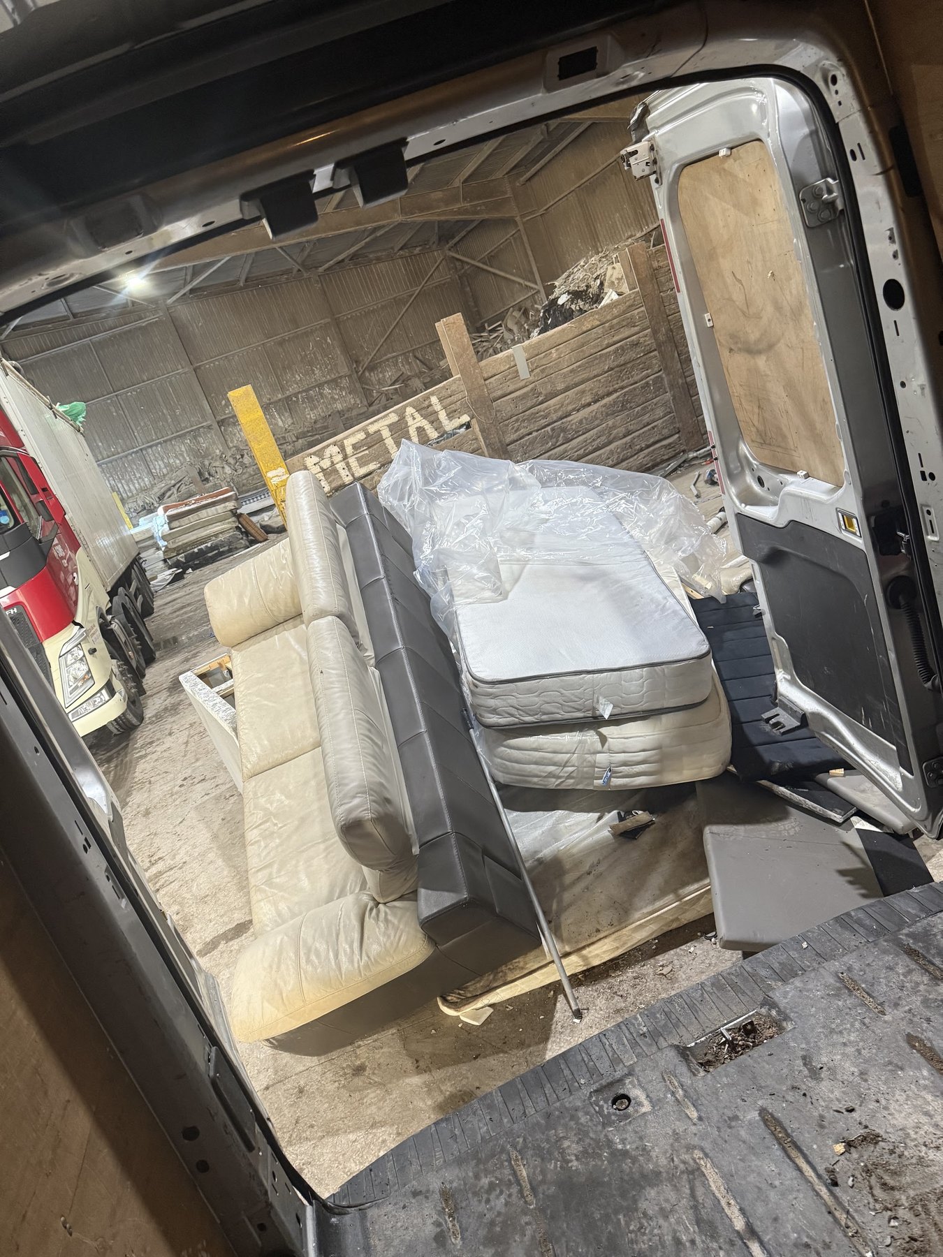 A sofa and a wrapped mattress loaded in the van, seen from the back doors